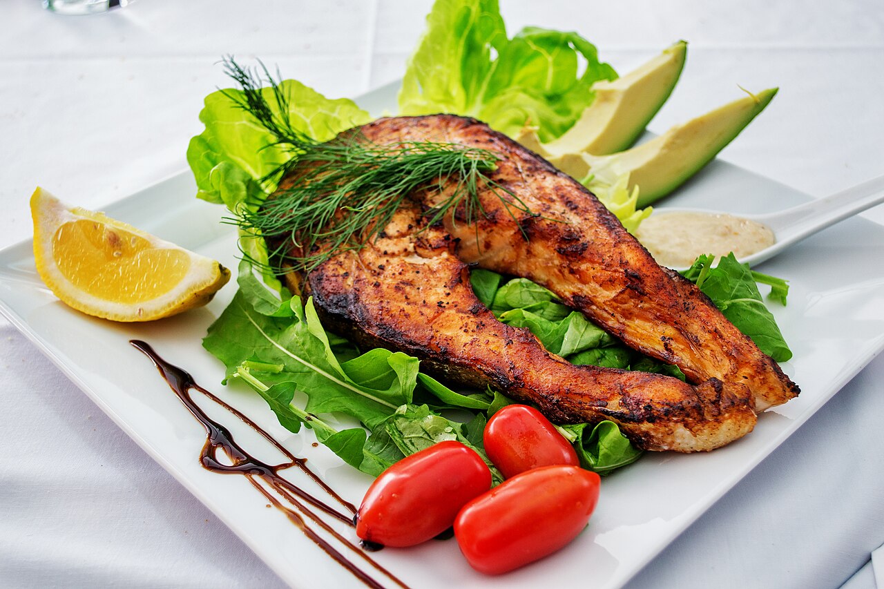 A grilled fish fillet on a plate with salad and lemon