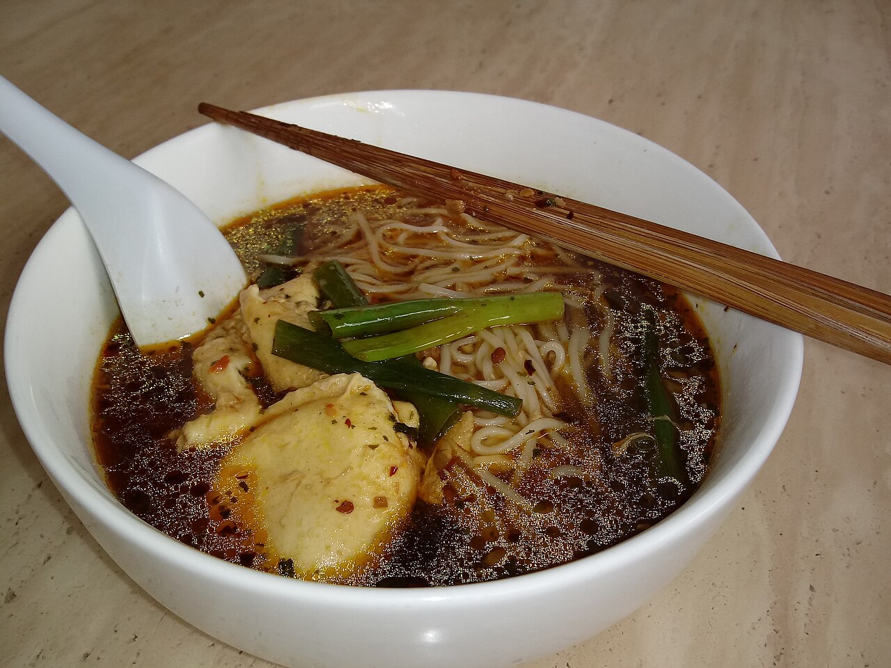 A bowl of noodles with chopsticks and a spoon