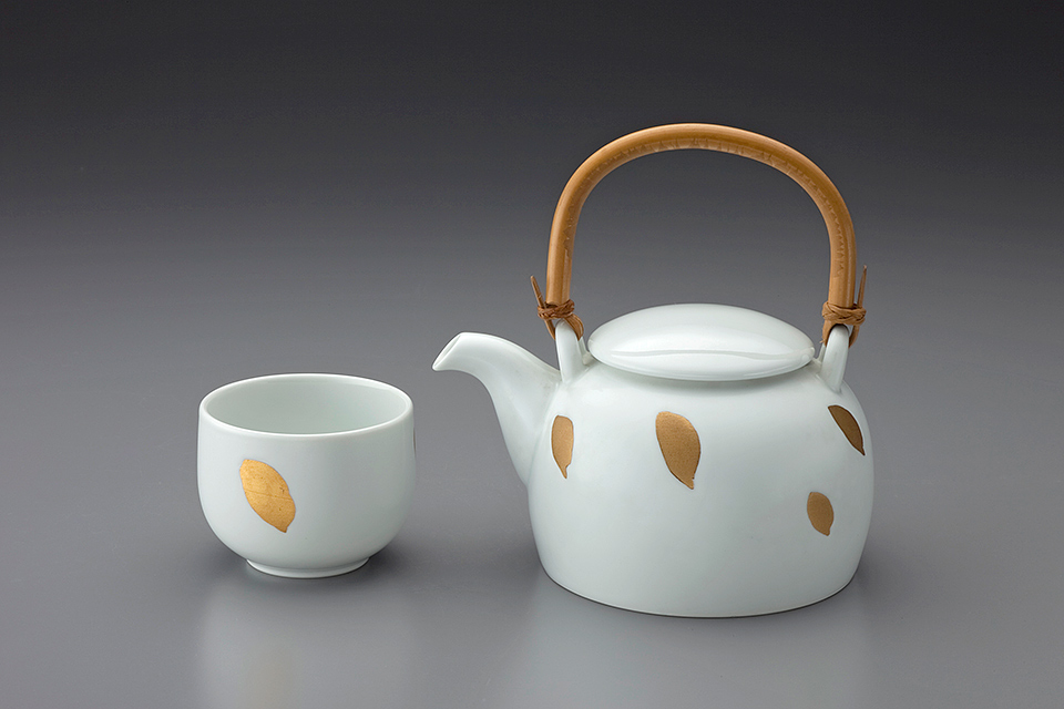 A white teapot with a bamboo handle and a white teacup